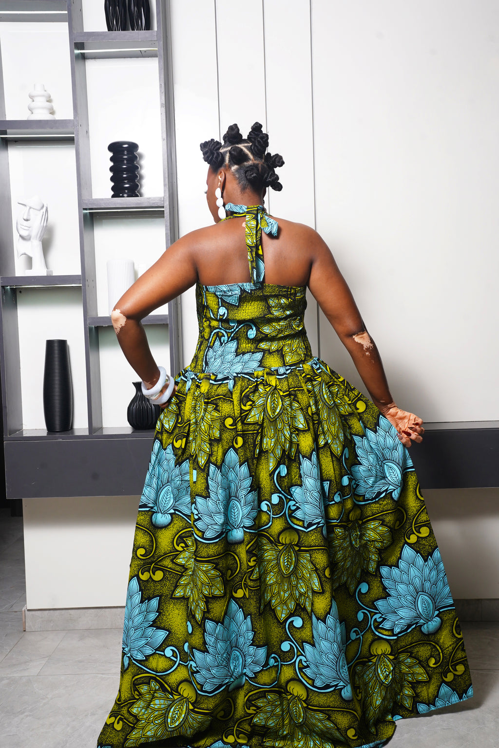 Woman wearing green and blue Ankara maxi dress by Selaro Luxury Wears shelves.