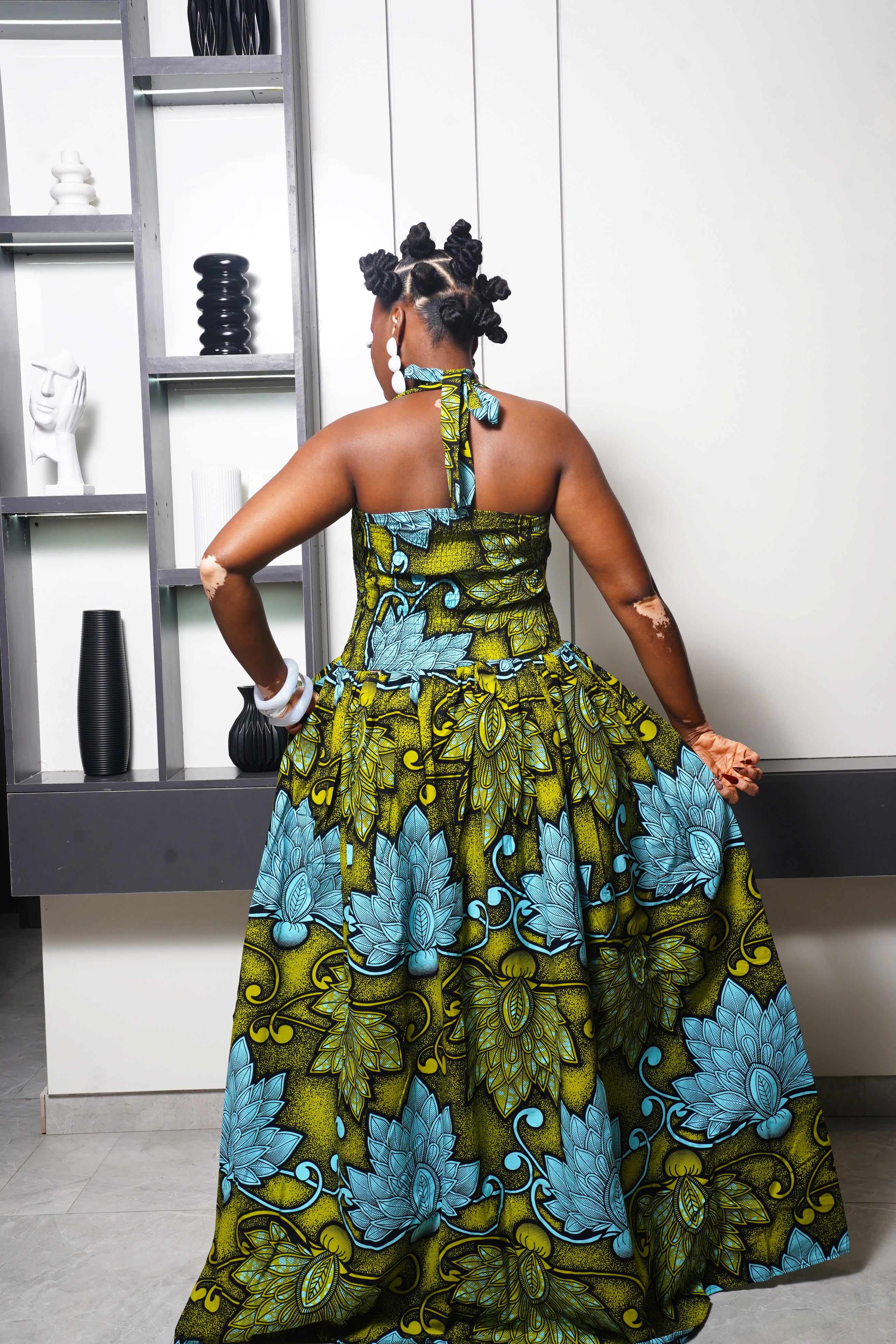 Woman wearing green and blue Ankara maxi dress by Selaro Luxury Wears shelves.