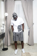White shirt with black brushstroke design styled with black‑and‑white striped shorts and matching cap.