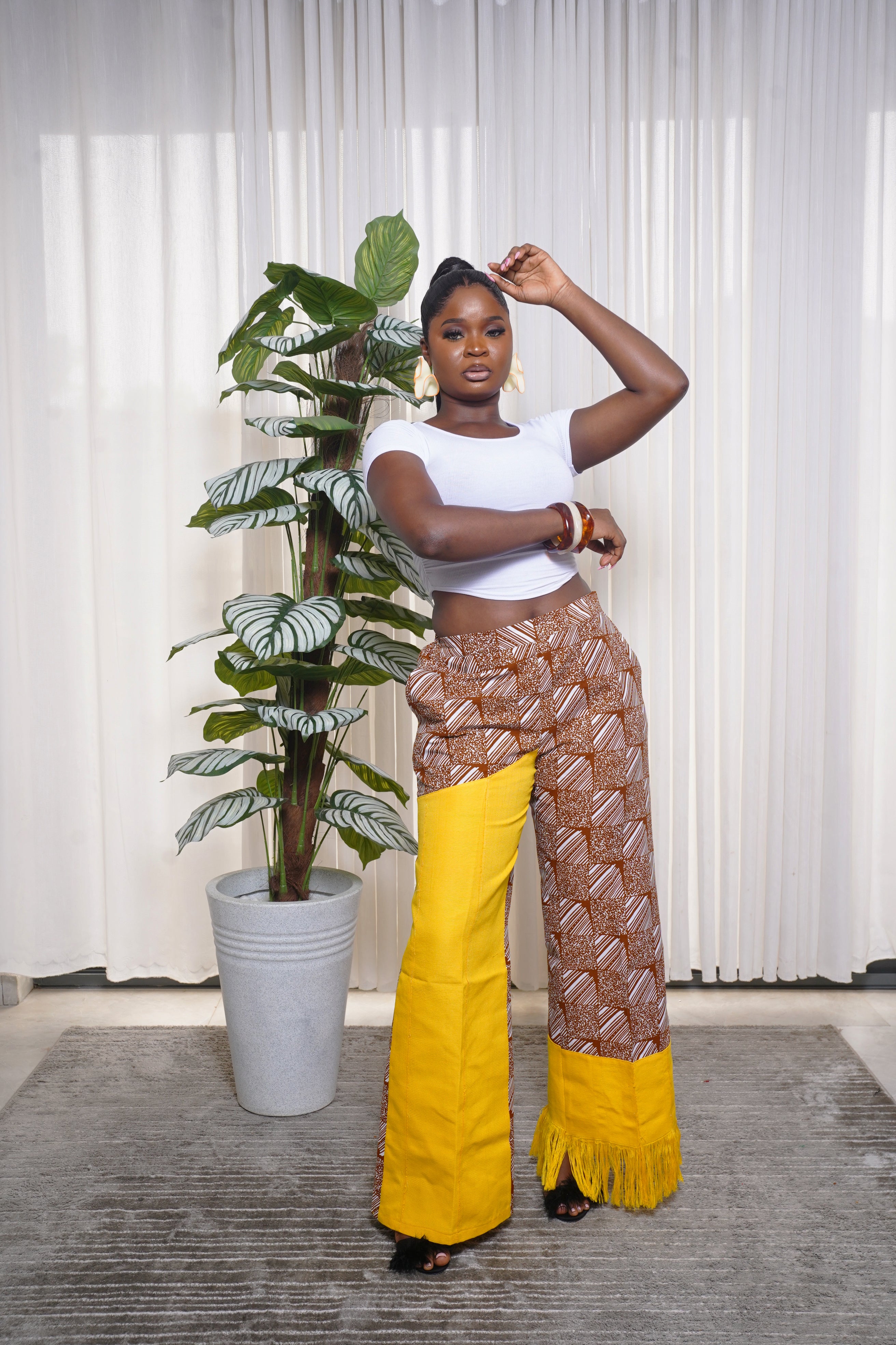 White crop top styled with brown African print pants featuring bright yellow fringe panels