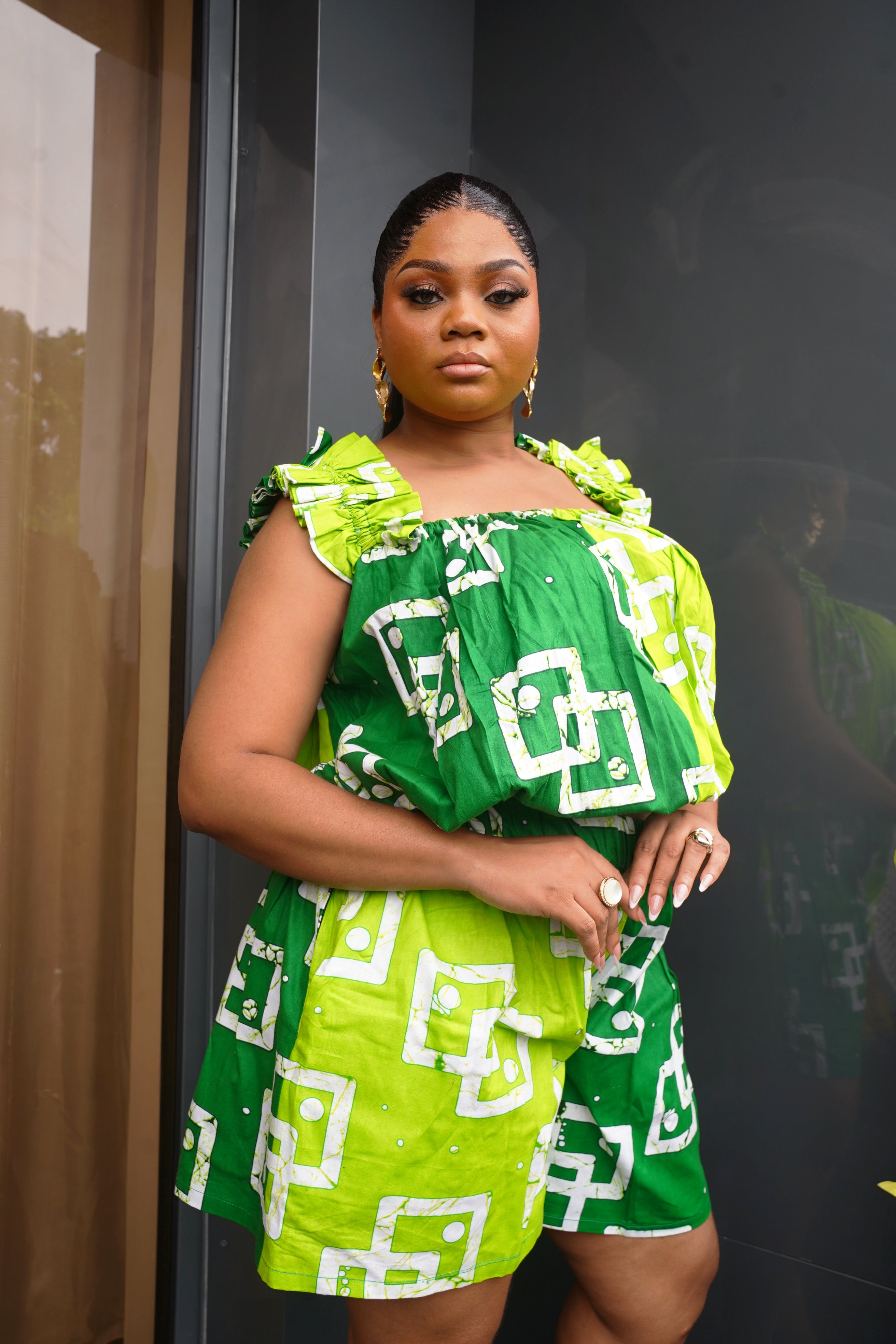 Bright green African geometric print ruffle‑sleeve top styled indoors with gold accessories