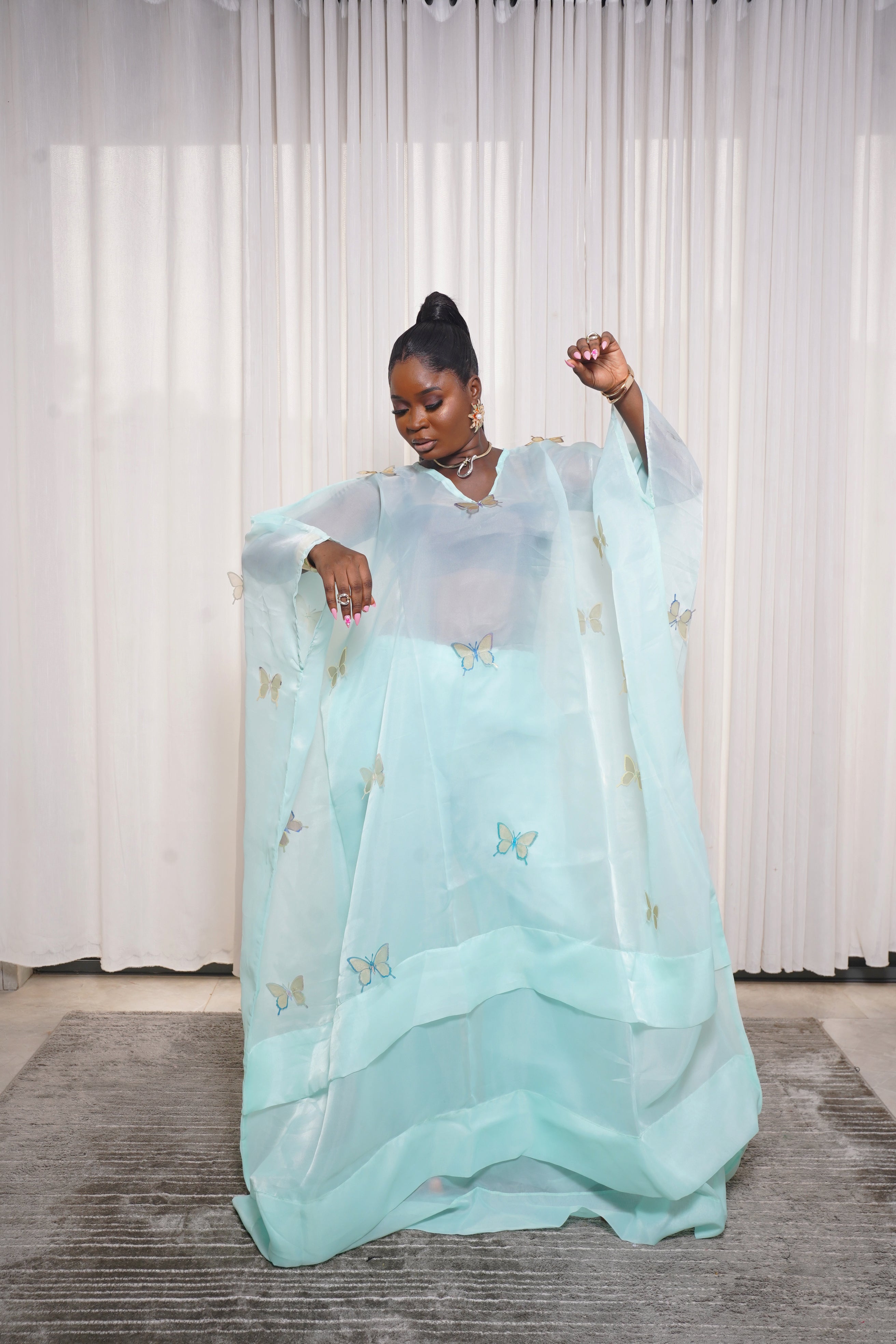 Flowing teal kaftan adorned with yellow‑green butterfly embroidery, styled with hoop earrings and necklace