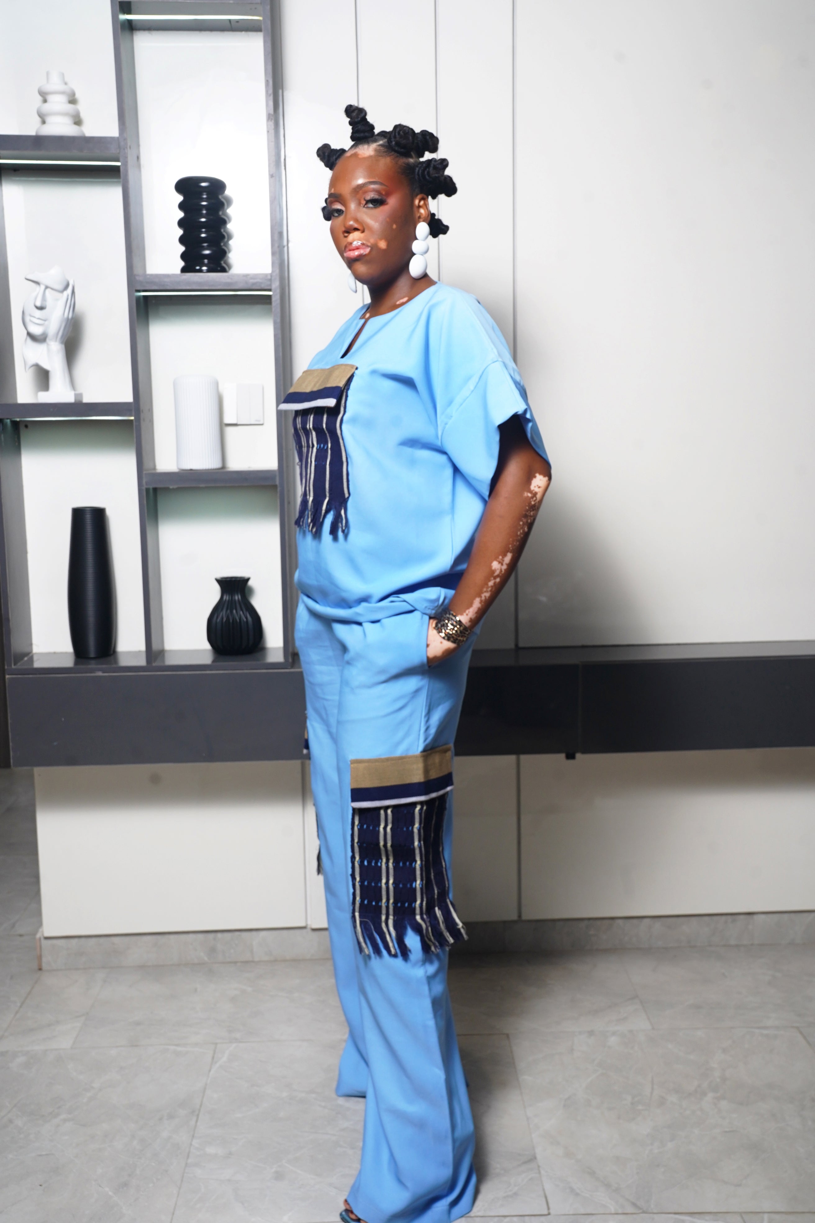 Model wearing light blue top and pants with woven striped fabric accents and white earrings
