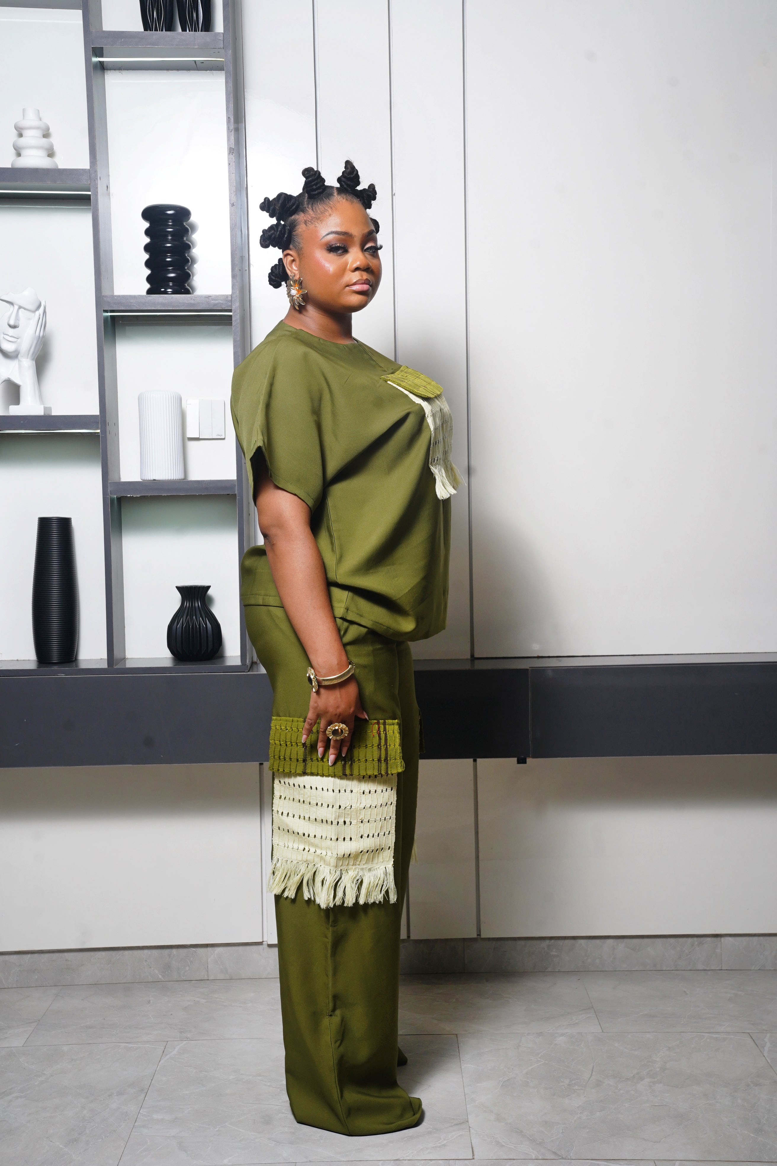 African olive green two‑piece outfit with woven cream fringe details styled with gold accessories