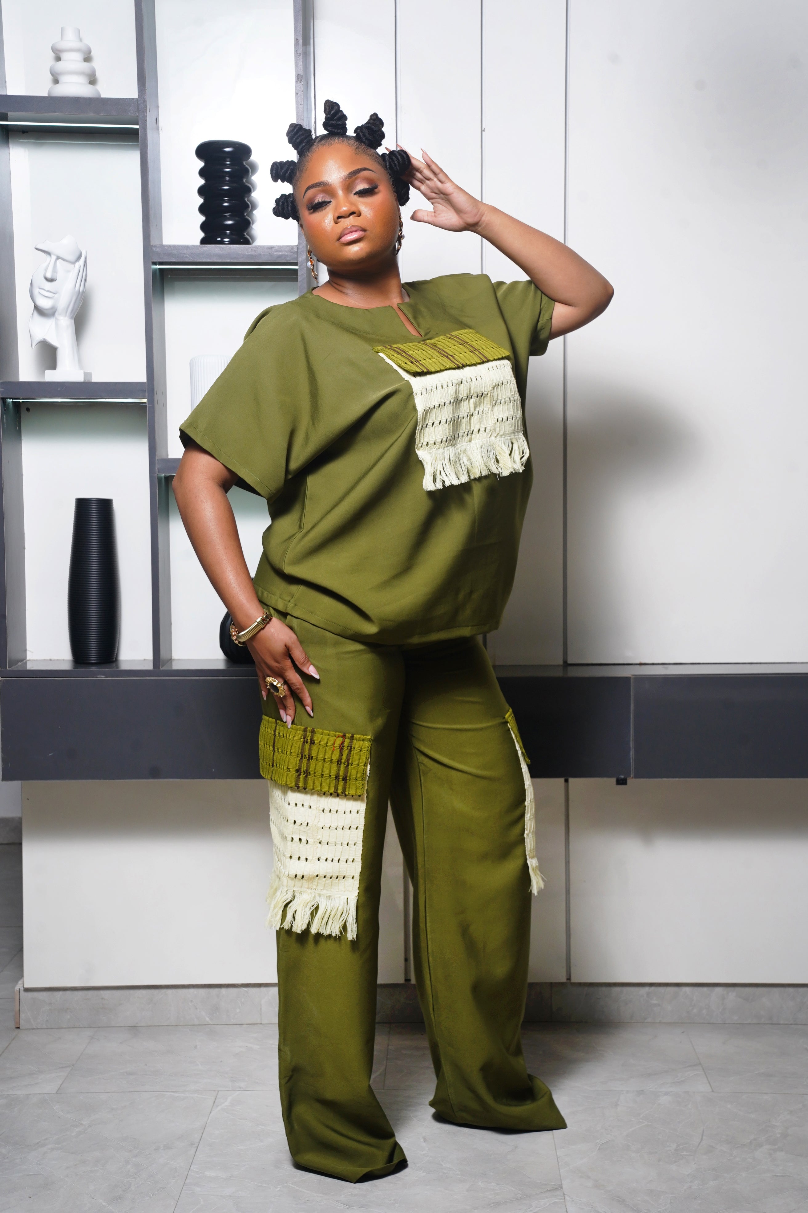 Model wearing olive green African inspired outfit with woven fringe accents in a modern interior