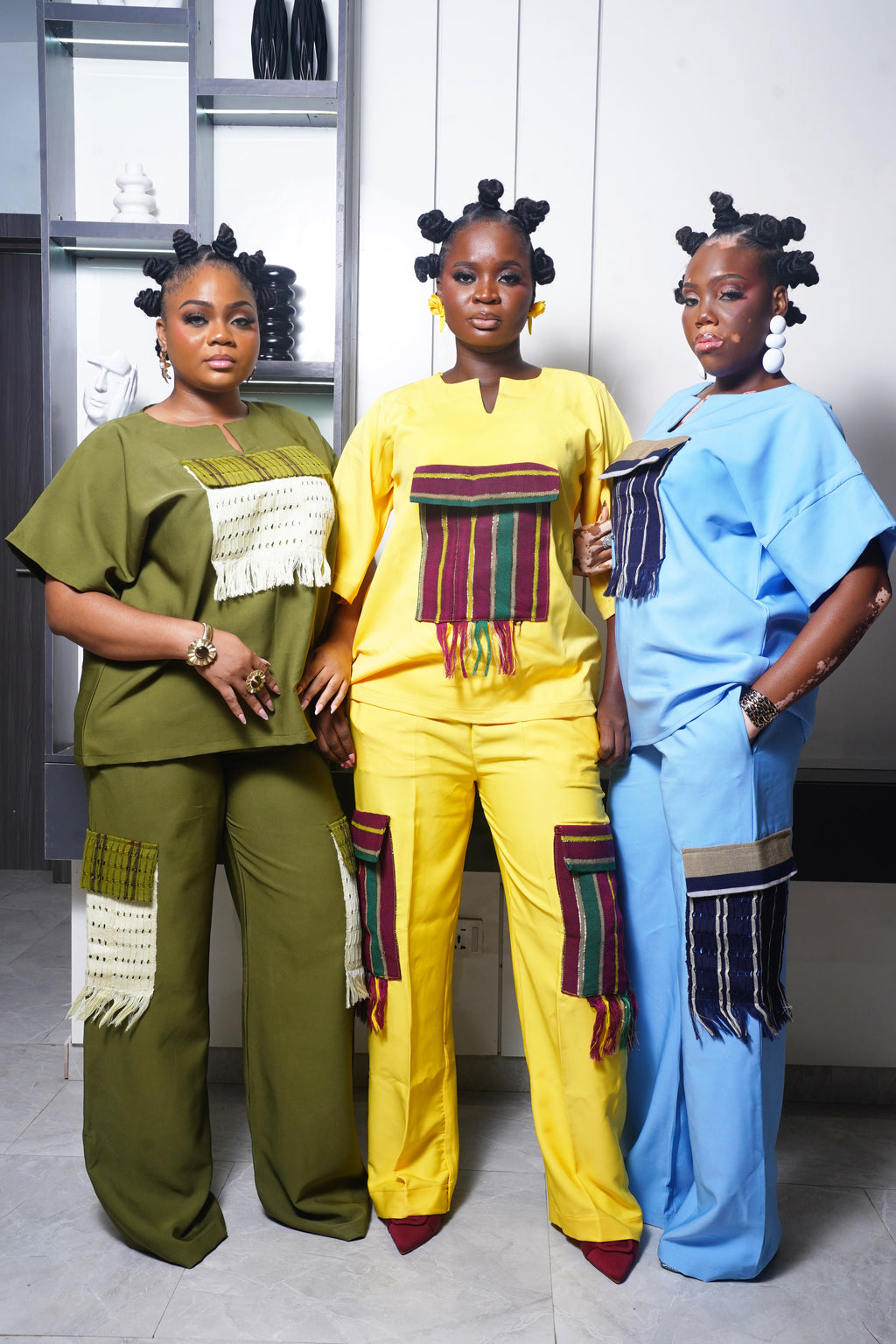 Model wearing olive green African inspired two‑piece outfit with woven cream fringe panels in a group fashion shot