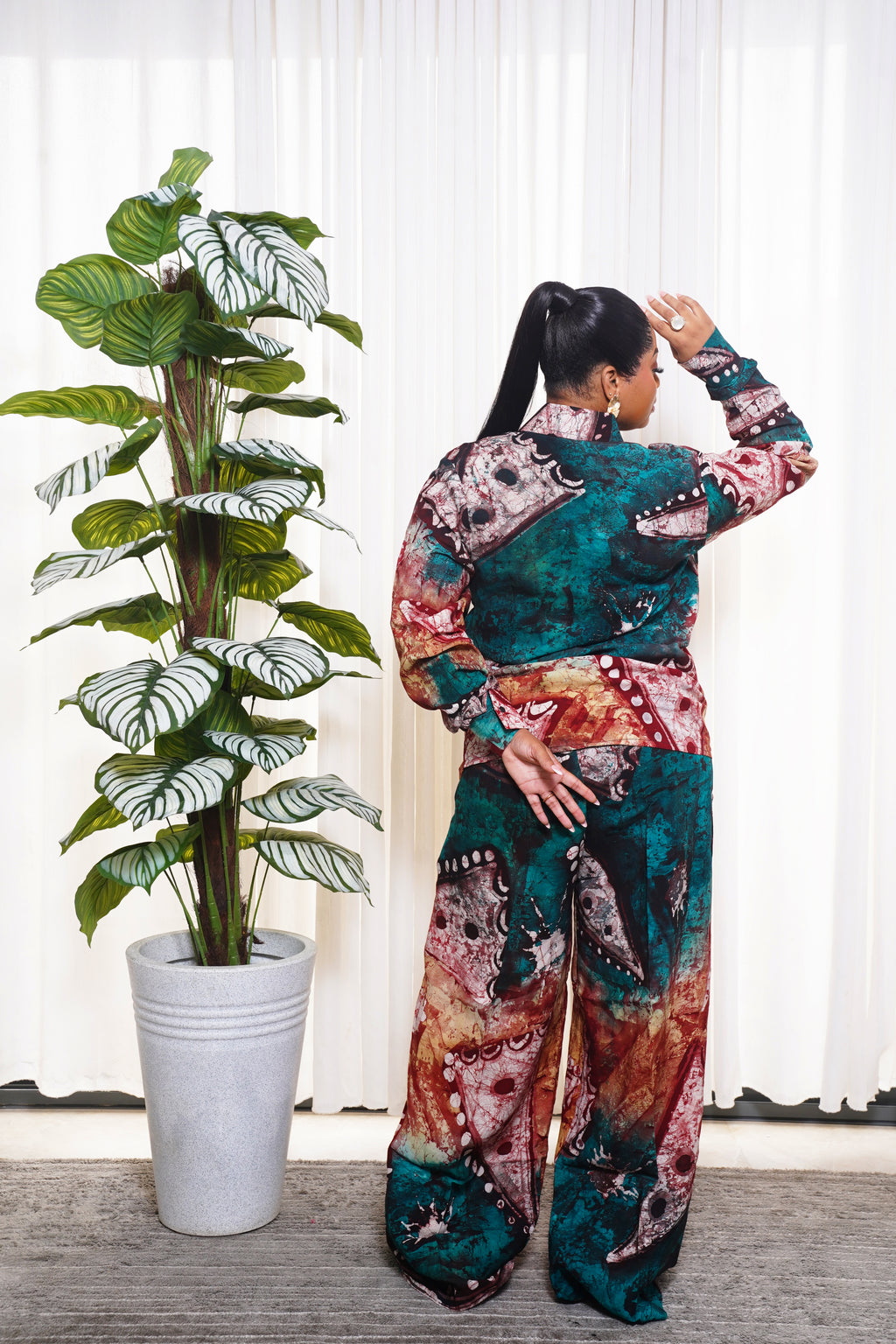 African abstract print two‑piece outfit in teal, brown, and beige tones styled indoors beside a tall plant
