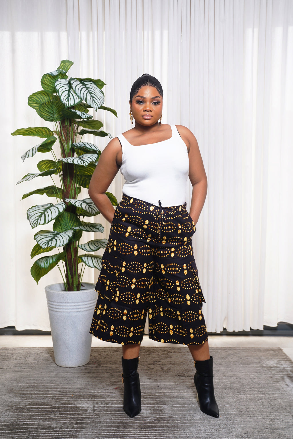 Model wearing white sleeveless top with black culotte pants featuring yellow and orange African circular motifs.