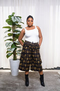 Model wearing white sleeveless top with black culotte pants featuring yellow and orange African circular motifs.