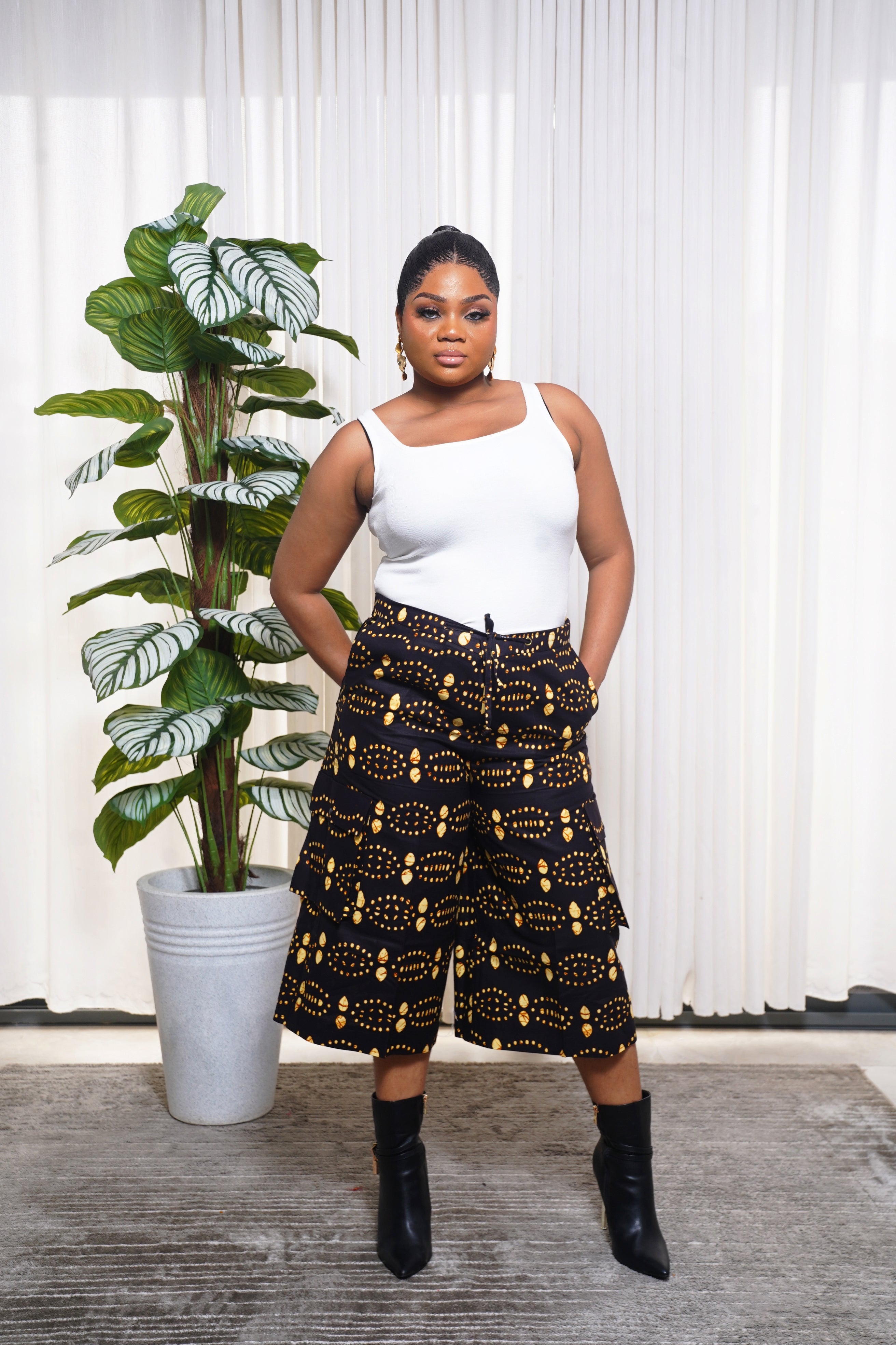 Model wearing white sleeveless top with black culotte pants featuring yellow and orange African circular motifs.