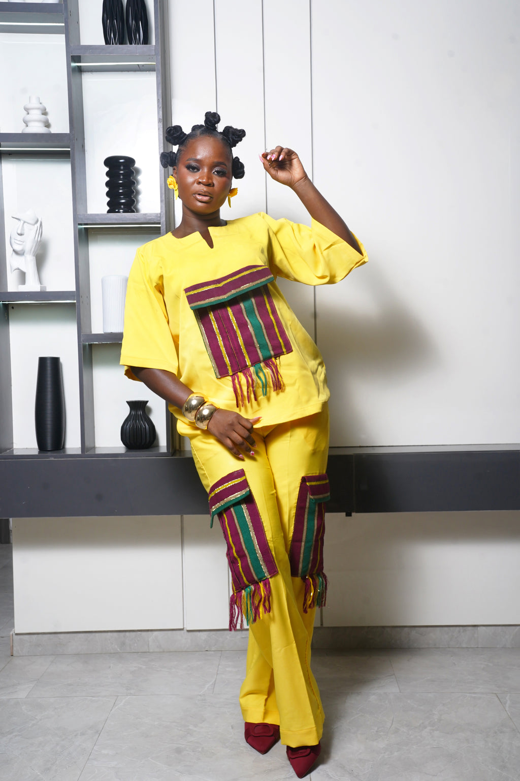 Bright yellow African two‑piece outfit with multicolored woven fringe panels and bold accessories
